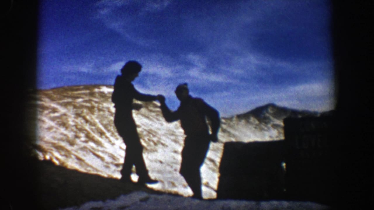 In metadata-supported 1961 Colorado footage, two bundled hikers appear in silhouette while holding hands on a snowy ridge.