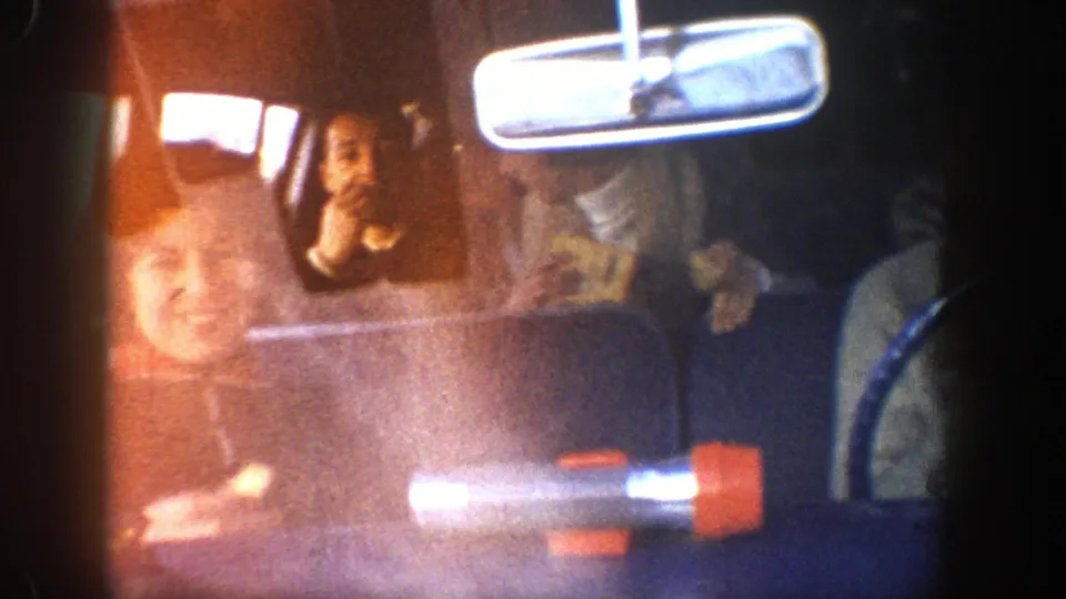 The 8mm frame shows multiple people inside the car, including a woman in the back seat eating, with strong light flare and the rearview mirror visible.