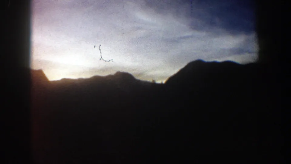 1961 Aspen, Colorado home-movie frame showing sunrise behind dark mountain ridges, with vertical obstruction and visible film wear.