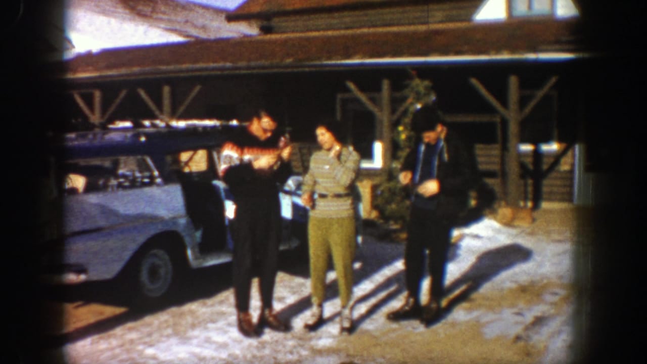 In 1961 Aspen, adults talk near an open white station wagon with roof gear outside a rustic lodge on snowy ground.