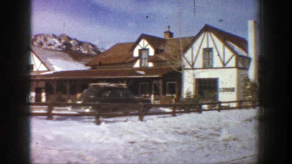 1961 Aspen resort lodge exterior with snowbanks, a parked station wagon, dark timber framing, and mountains behind.