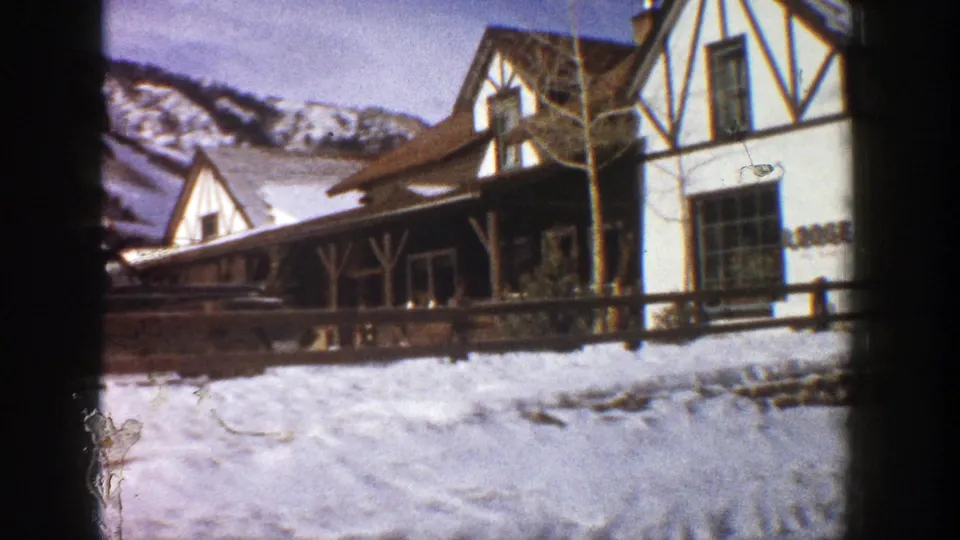 Closer 1961 Aspen lodge view with snow in the foreground, timber details, bare trees, fencing, and mountain terrain behind.