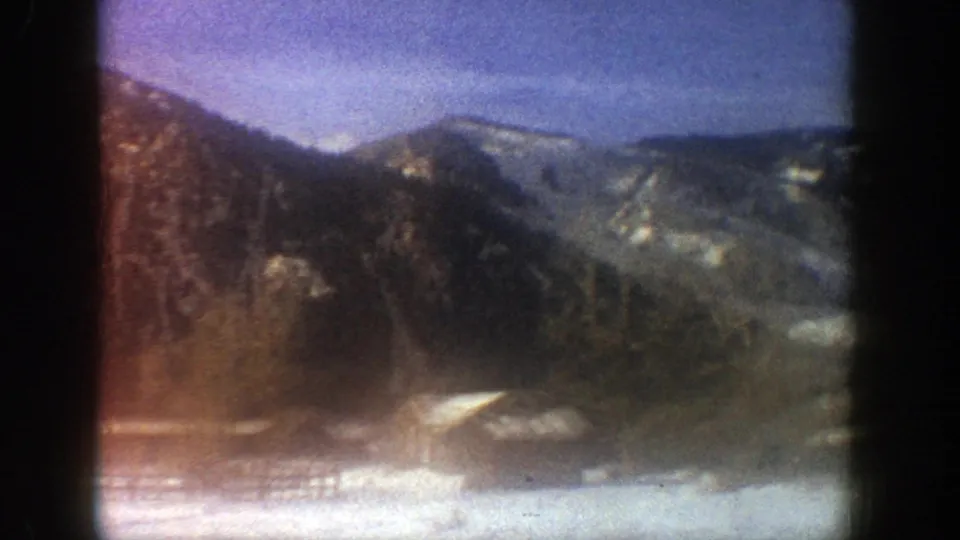 1961 Aspen mountain view with snow at the bottom of frame, wooded slopes, and hazy ridgelines beyond.