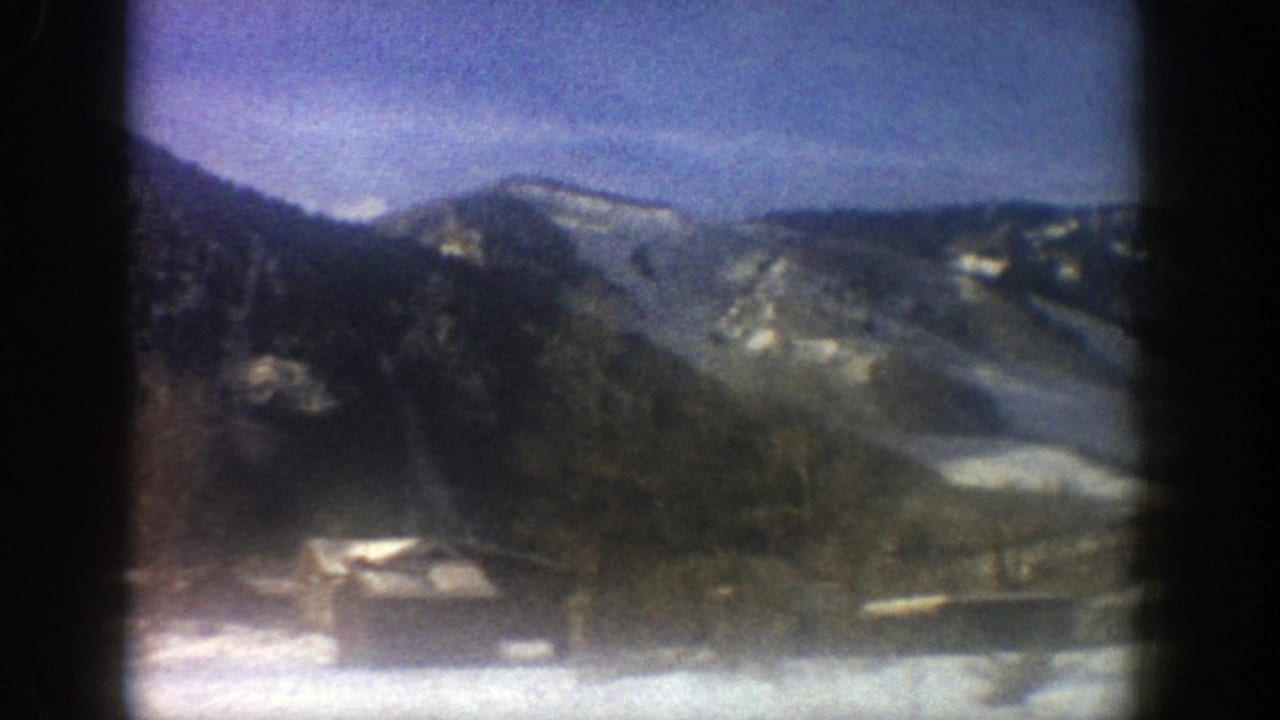 Snowy mountain slopes above cabins and trees under a blue sky.