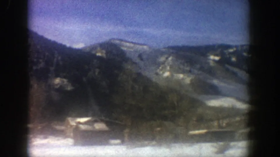 1961 Aspen, Colorado home-movie view of snow-dusted mountains, dark trees, low cabins, and a bright winter sky.