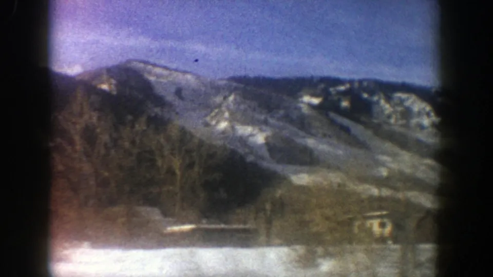 Aspen mountain ridge in 1961 8mm footage, with patchy snow, winter trees, and low buildings in the valley.