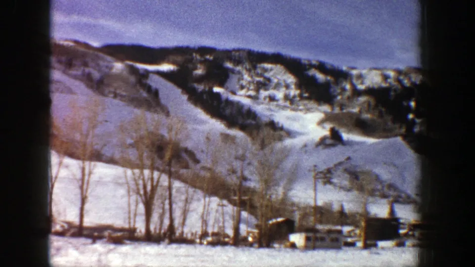 Aspen winter landscape frame with snow-covered ridges, leafless trees, utility poles, and low valley structures.