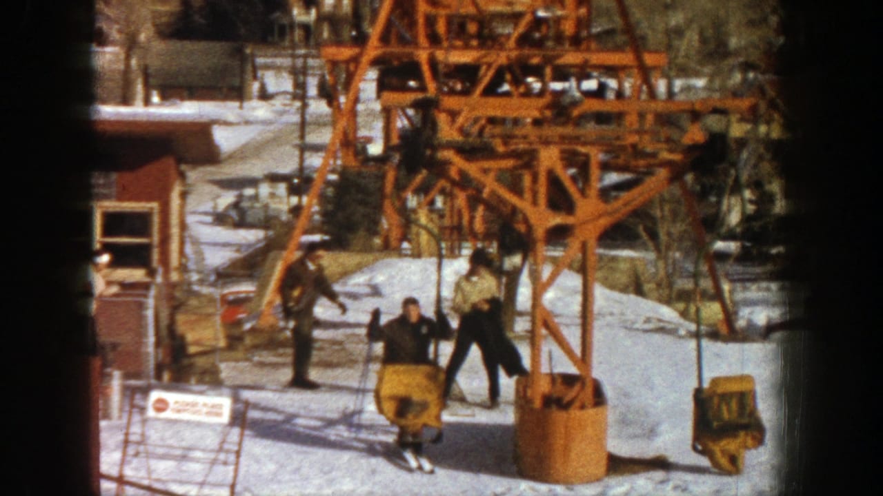 Skiers gather near a yellow chair below an orange ski lift tower in snow.