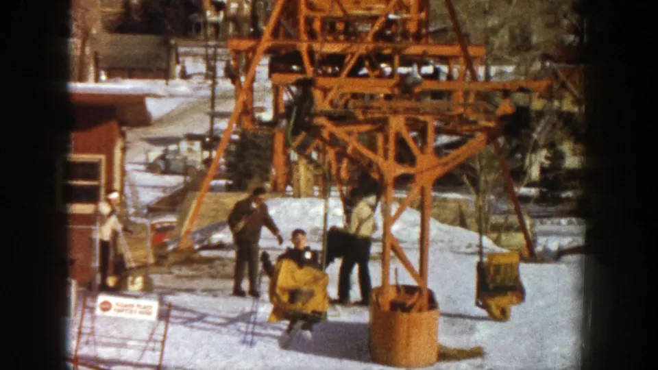 Skiers in winter clothing stand by a yellow chairlift carrier at an Aspen, Colorado ski area in 1961.