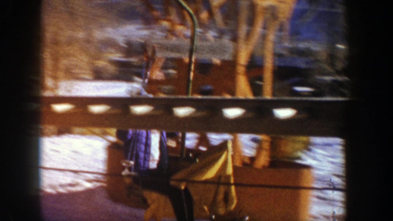 Partial view through a wood railing of a bundled chairlift rider over snow.