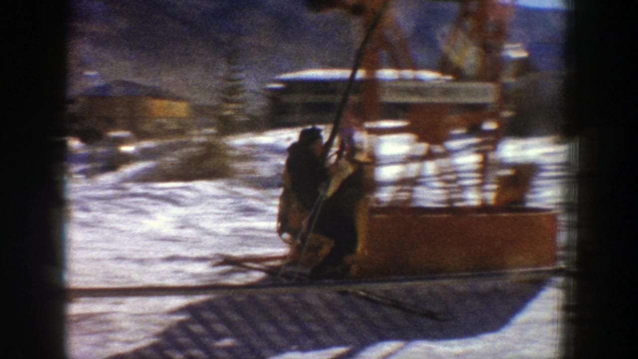 In 1961 Aspen, Colorado, a skier appears near a chairlift loading area on snow, with lift equipment, resort structures, trees, and mountain slopes in the background.