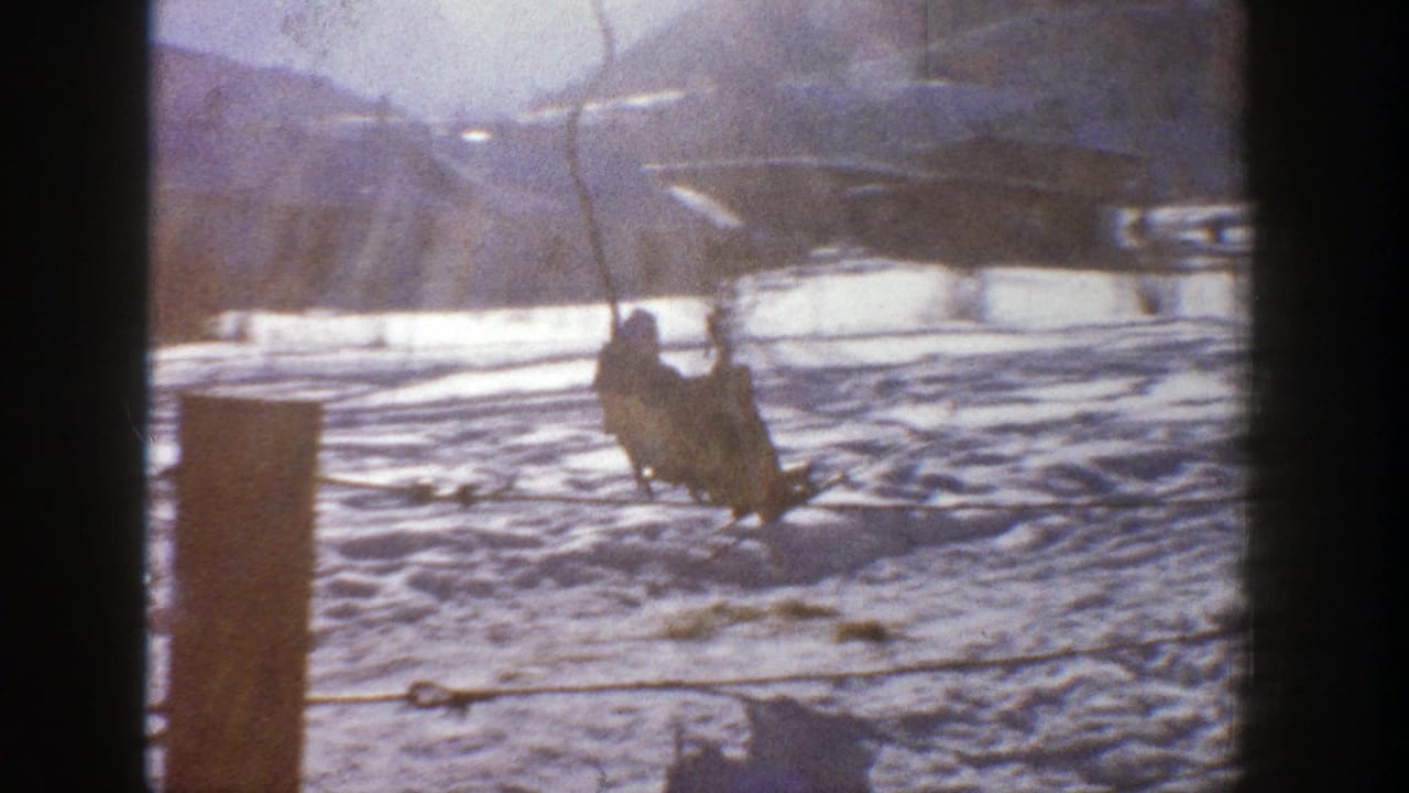 A person rides a suspended chairlift above a snowy slope with mountains in the distance.