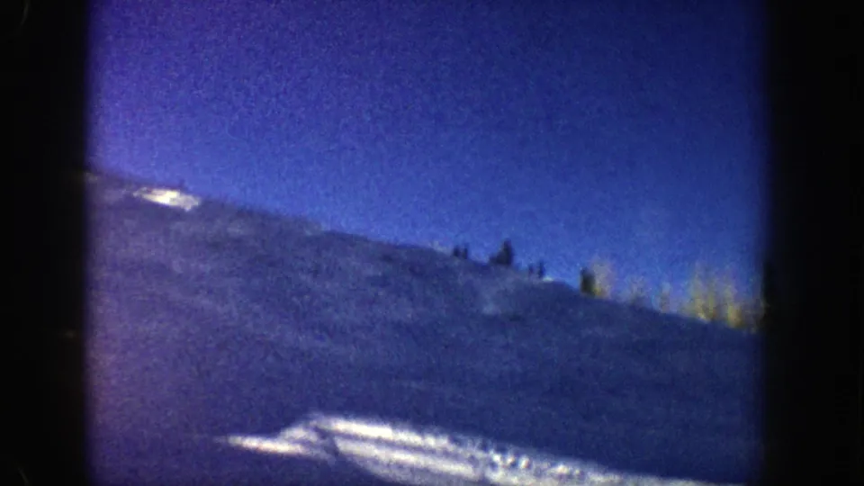 The closing frame continues the elevated Aspen mountain view, showing snowfields, scattered conifers, and strong blue 8mm color across the slope and sky.