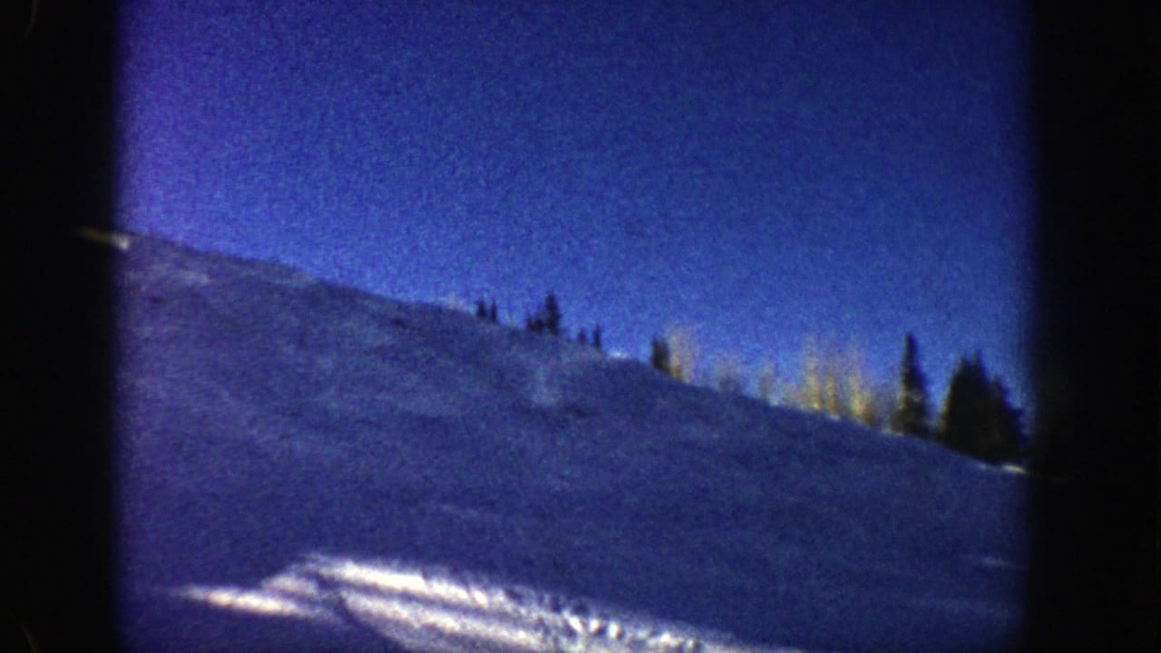 Snowy hillside under a deep blue sky with scattered trees near the ridge.