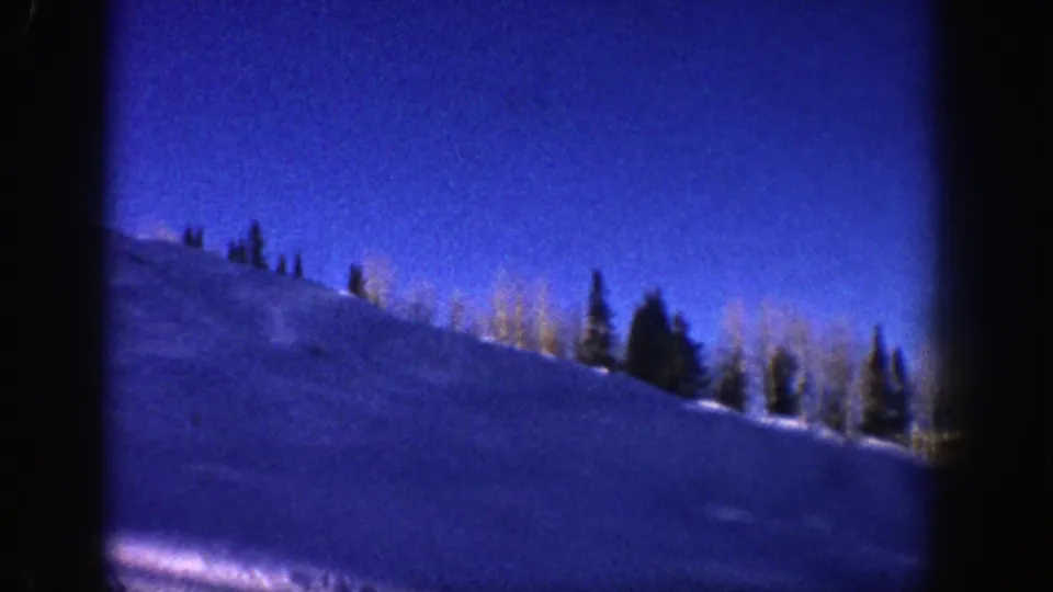 1961 Aspen frame of a snow-covered slope with evergreens and bare aspens along the crest, seen through dark 8mm frame edges.