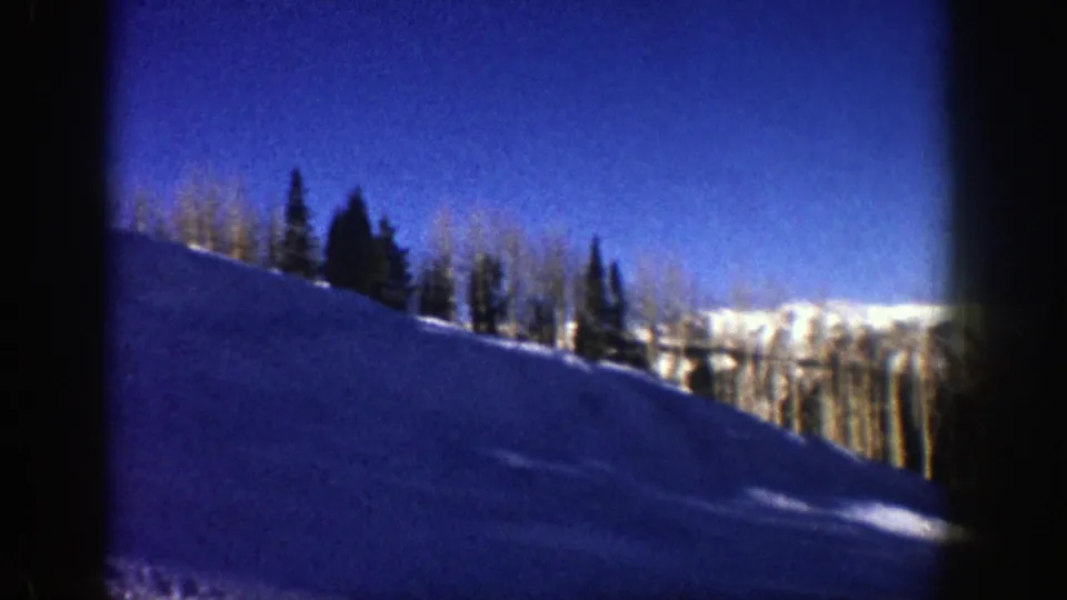 1961 Aspen home-movie view across a snow-covered hillside, with aspens, evergreens, and distant mountain peaks entering the frame.