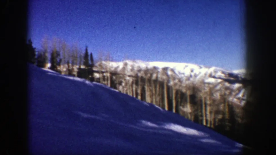 1961 Aspen frame showing a shadowed snow slope, leafless aspens, evergreens, and sunlit mountain ridges in the background.