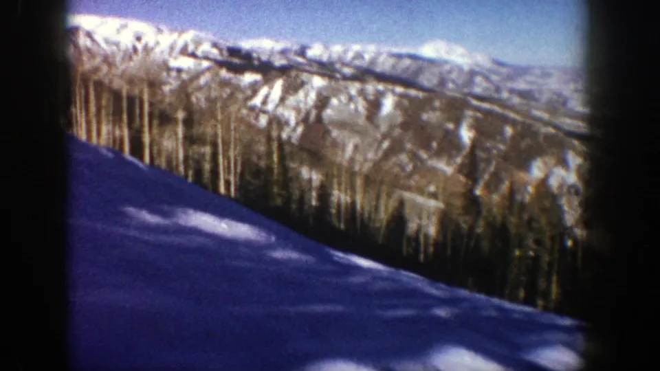 1961 Aspen home-movie frame with a shaded snow slope, dense trees, and sunlit mountain ridges.