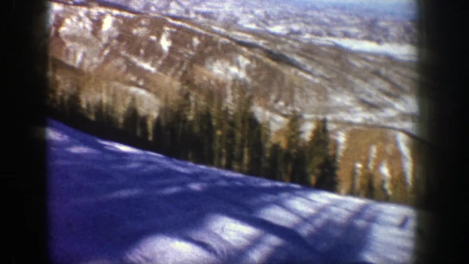1961 Aspen 8mm frame looking across snow, forest, and a distant mountain valley in winter light.