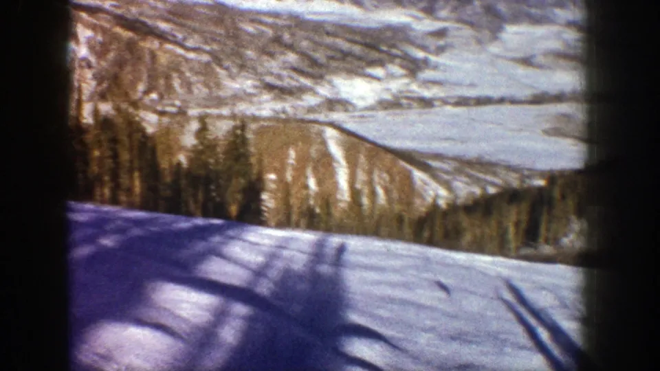 1961 Aspen frame showing a snow-covered downhill foreground, dark tree shadows, forest, and distant valley contours.