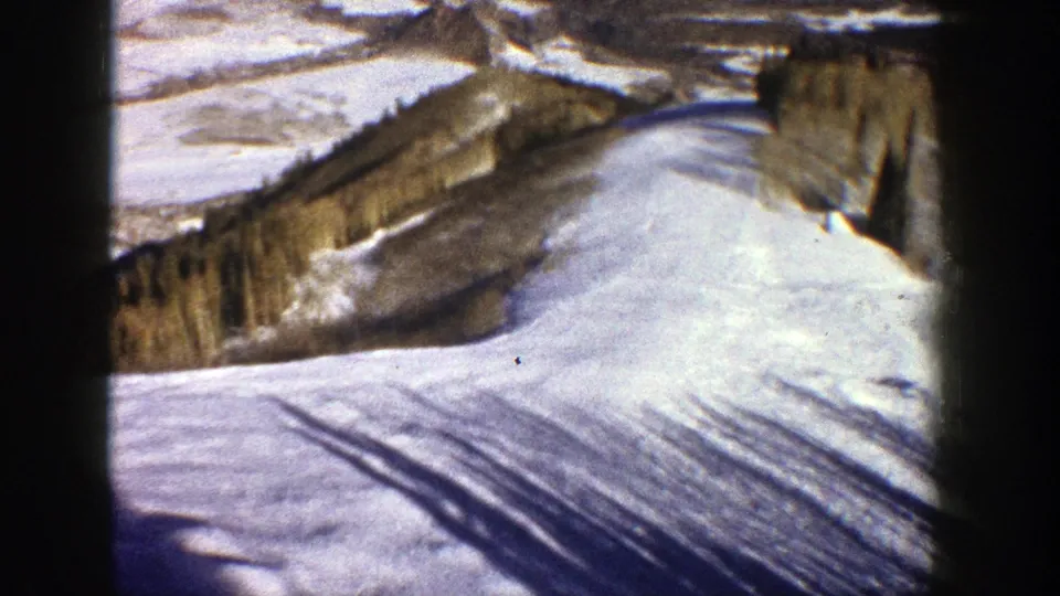 1961 Aspen home-movie frame showing a broad snow slope, long shadows or tracks, trees, and a mountain ridge in winter light.