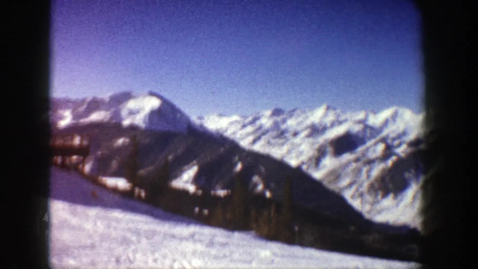 1961 Aspen 8mm view of a bright snowfield, dark ridge, and distant alpine peaks with a cropped building at left.