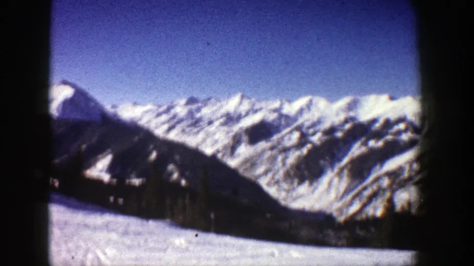 1961 Aspen home-movie frame showing a wide sweep of snow-covered Rocky Mountain ridges and blue sky.