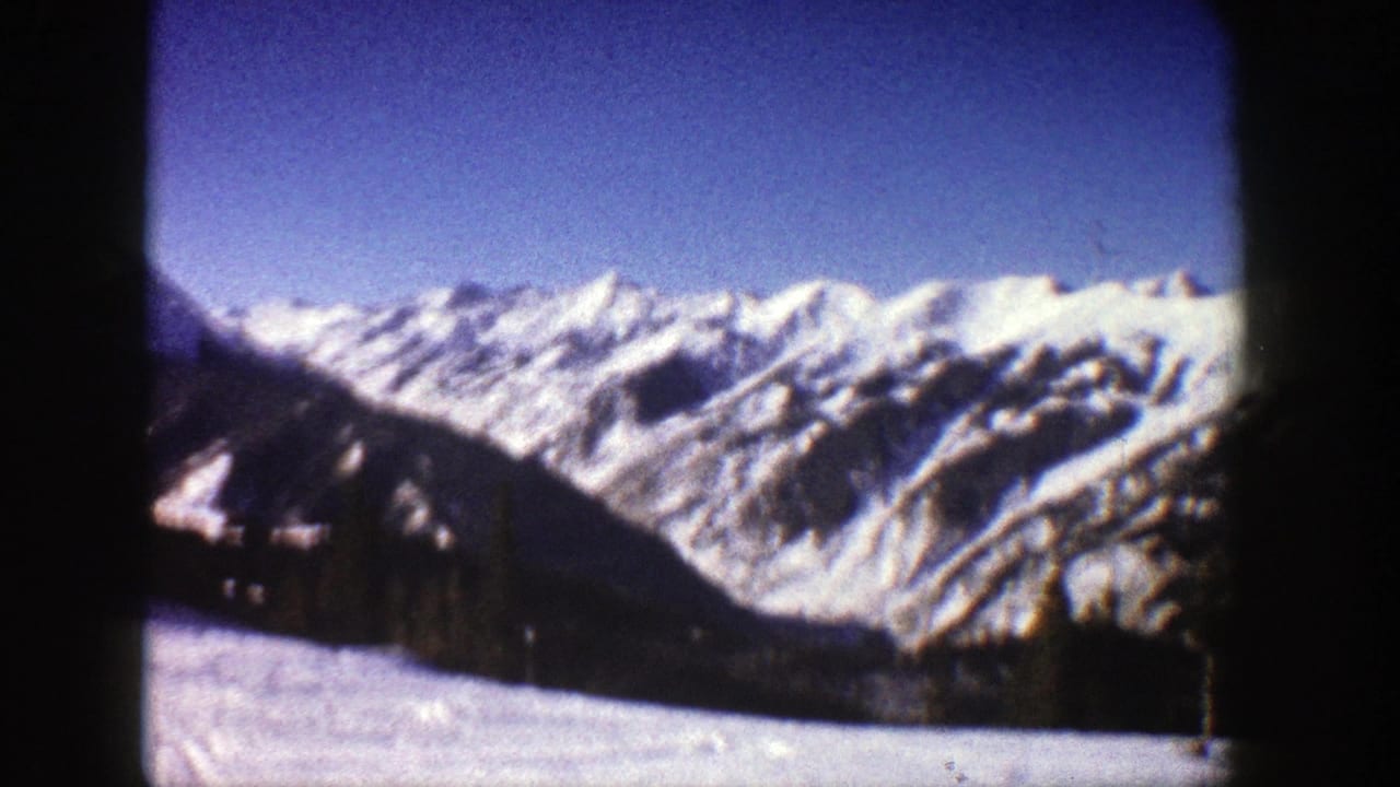 1961 8mm frame likely near Aspen, Colorado, showing snowy mountain peaks, shadowed lower slopes, and a clear blue sky.