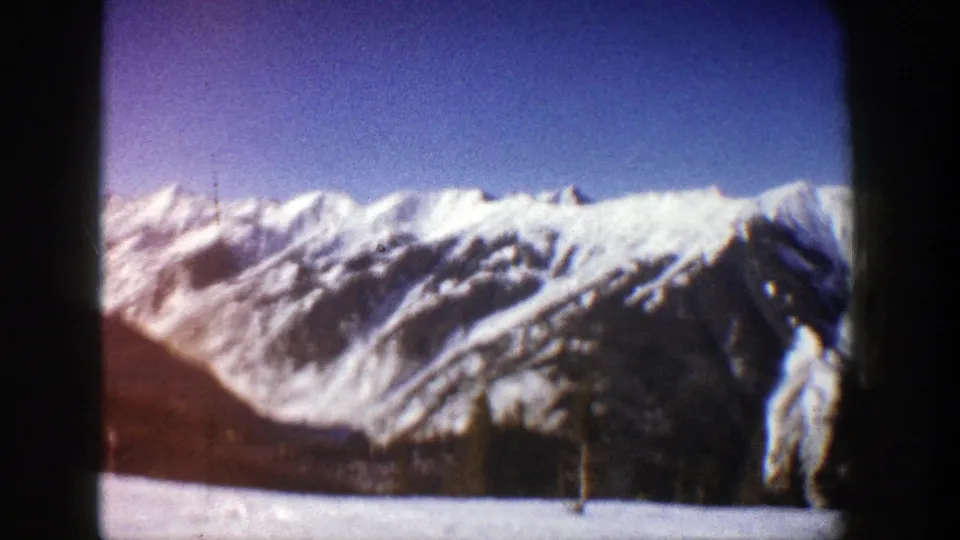 1961 home-movie frame likely near Aspen, Colorado, showing a broad snowy ridge, evergreen trees, and a bright snowfield below.