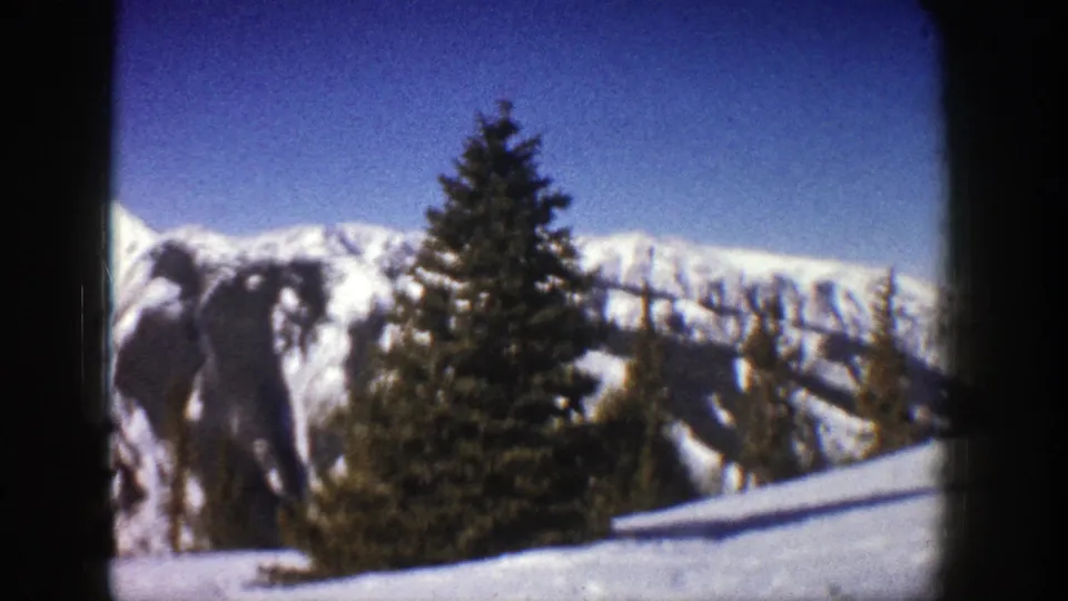 1961 Aspen, Colorado home-movie frame with evergreen trees against a bright winter mountain range.