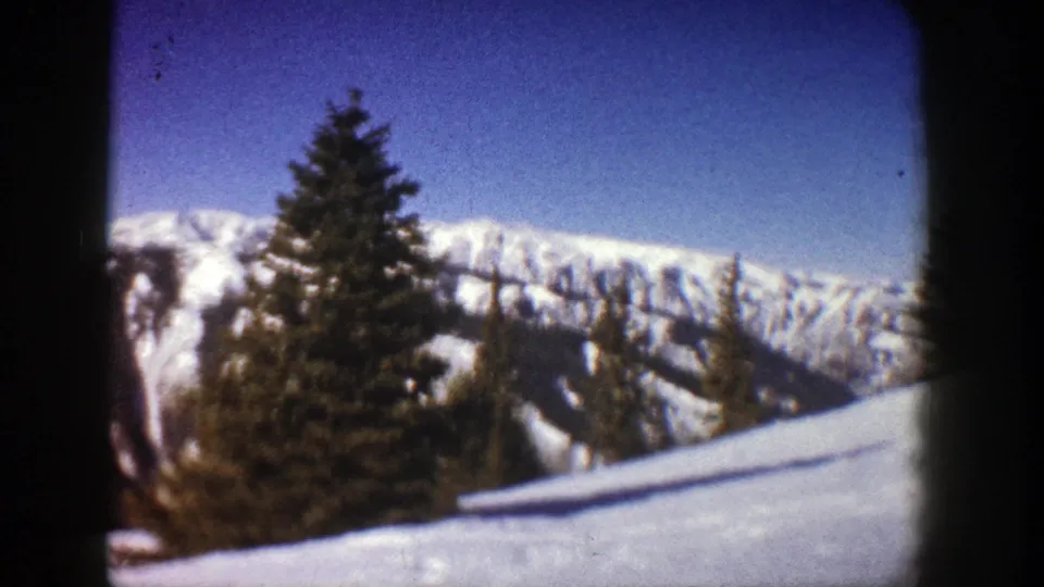 1961 Aspen, Colorado 8mm frame showing a snowy foreground slope with evergreens and distant mountain ridges.