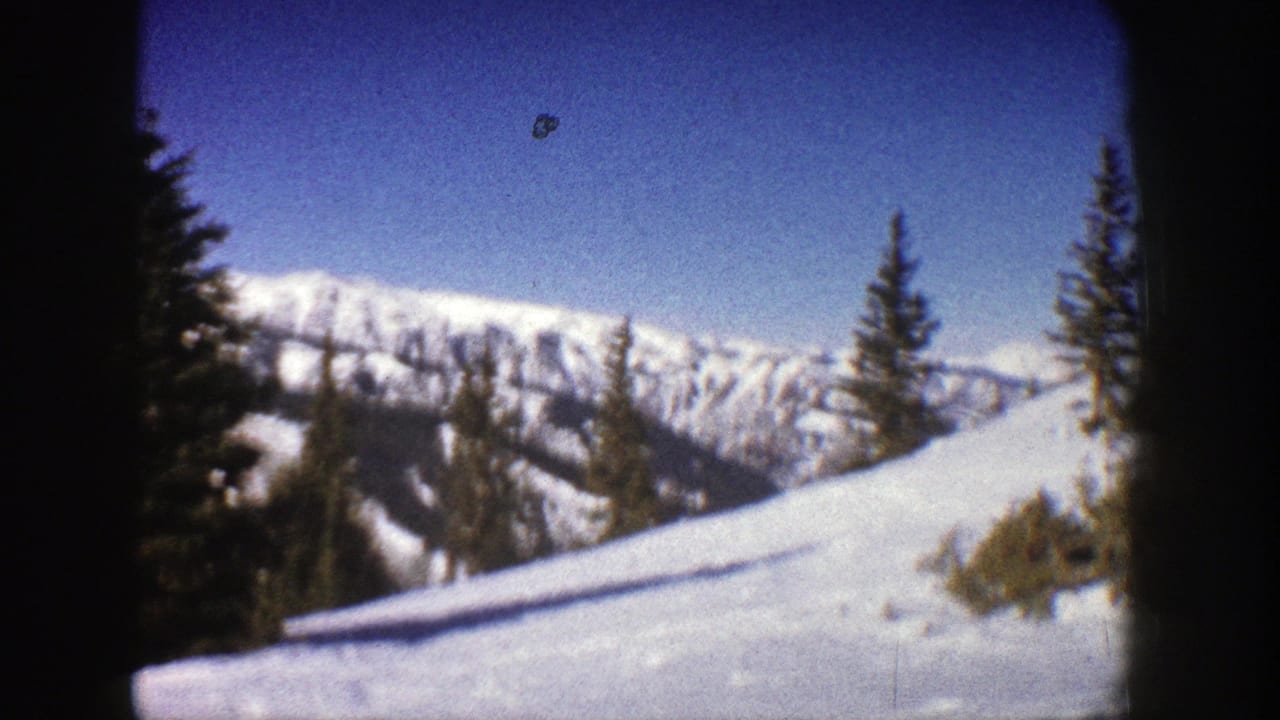 1961 Aspen, Colorado home-movie frame showing snow-covered alpine terrain, evergreens, and distant ridgelines through an 8mm film gate.