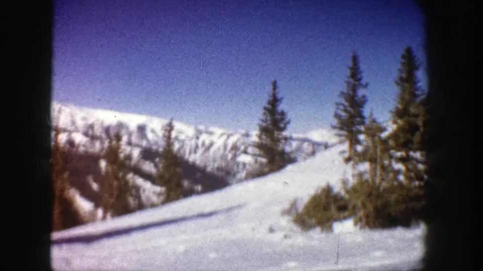 Aspen winter landscape from 1961 home-movie footage, with bright snow, conifers, and mountain ridges in a handheld 8mm frame.