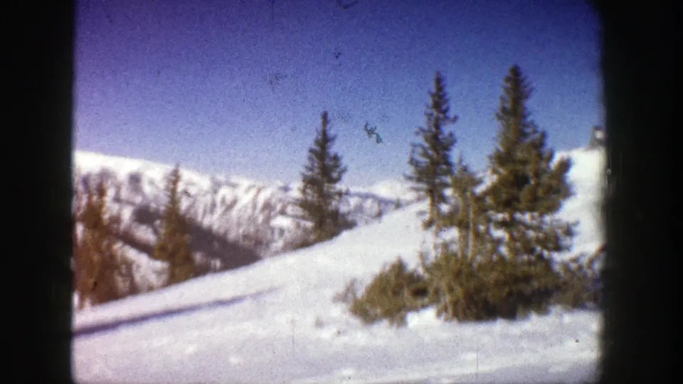 Handheld 8mm view of Aspen snowfields, conifers, and distant mountains, with visible grain and softened color from the 1961 film scan.