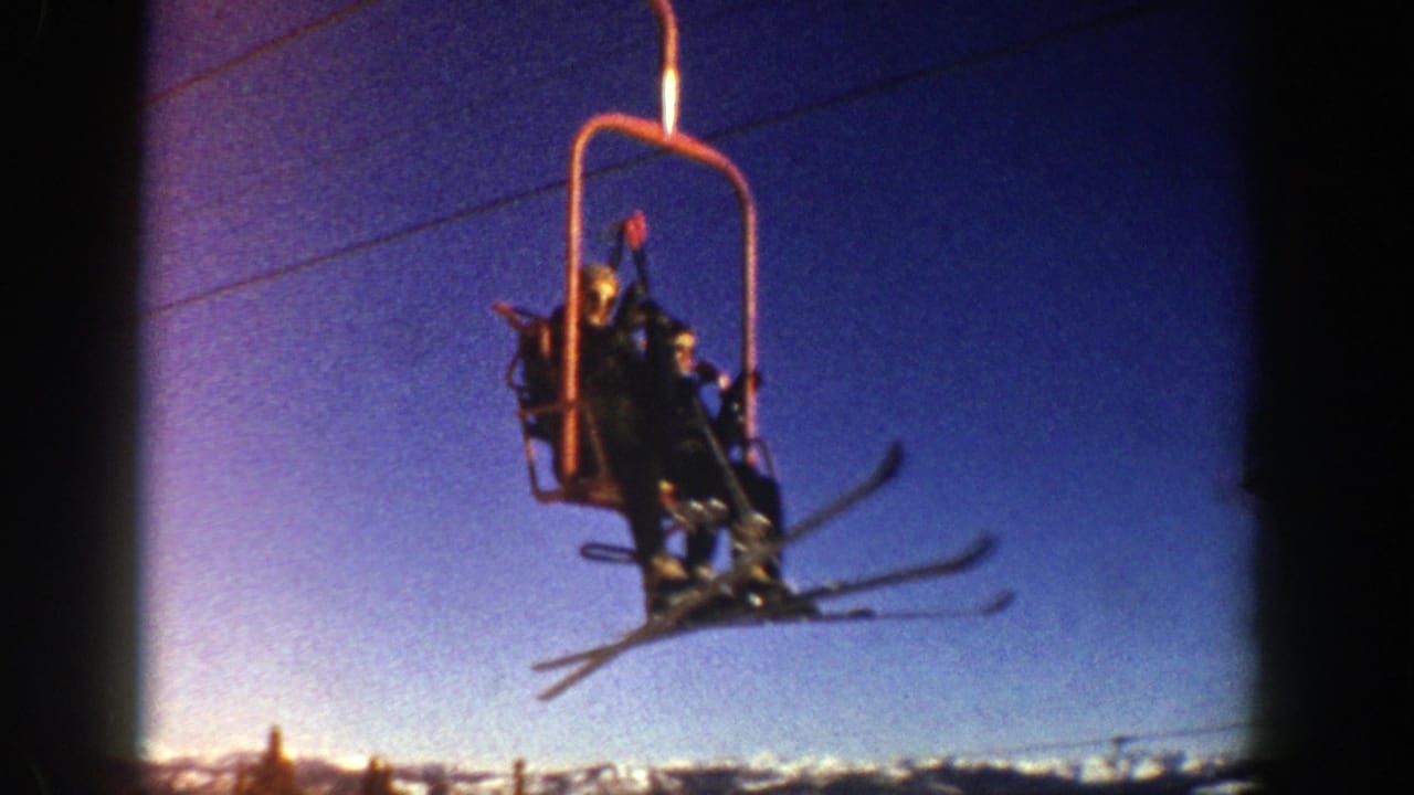 Chairlift riders move closer to the camera with skis visible below the chair.