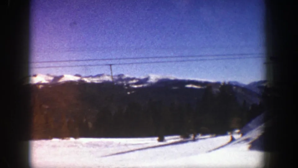 The view shifts to the Aspen ski area landscape in 1961, showing a bright snowy slope, dark trees, lift cables, and distant mountain ridges under a blue sky.