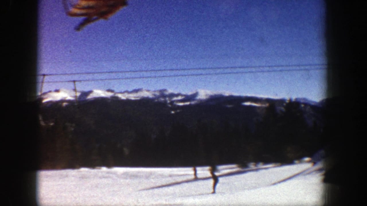 Skiers on a snowy slope below a lift cable with mountains in the background.