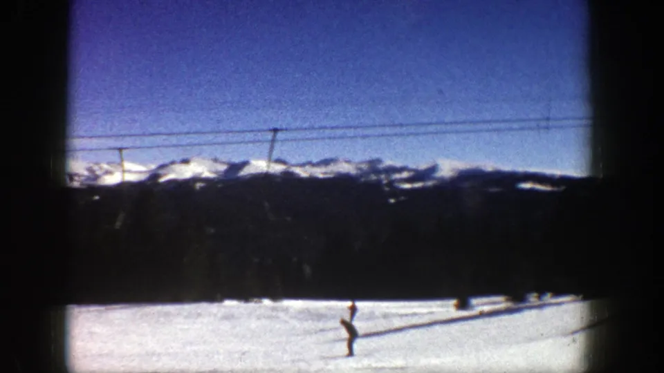 1961 Aspen winter scene showing a skier on an open slope below a ski lift cable, with evergreen trees and snowy mountains behind.