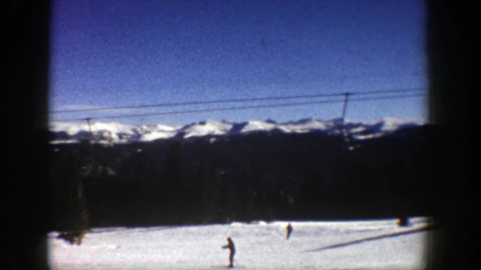 Aspen, Colorado ski-resort footage from 1961 with several distant skiers on snow below lift cables and a mountain horizon.