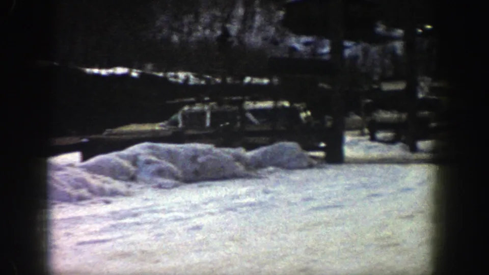 A station wagon travels or stands near roadside snowbanks in the Aspen winter scene, with trees behind it.