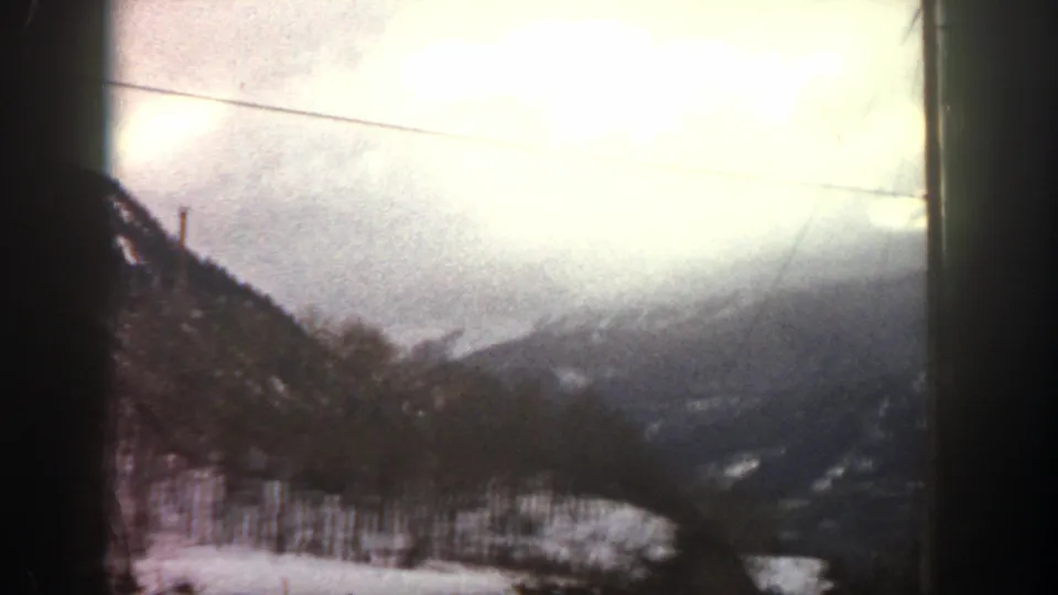 1961 Aspen, Colorado 8mm frame showing snow-covered trees and mountain ridges under a bright overcast sky, seen from a moving vehicle.