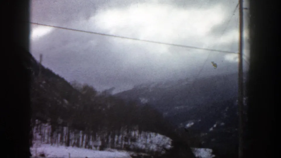 1961 Aspen, Colorado winter landscape with a utility pole and overhead wire crossing snowy wooded foothills and clouded mountain ridges.
