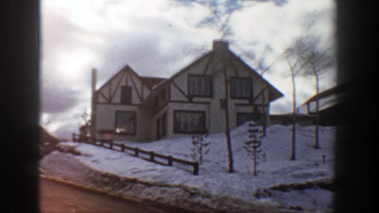 Snowy road passing a Tudor-style house with timber framing and bare trees.