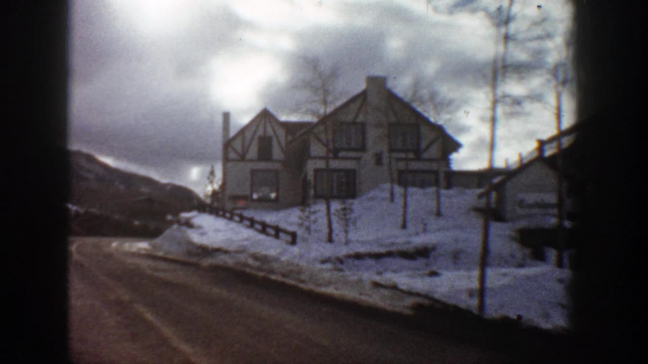 Snow-covered roadside with a large timber-framed house and distant mountain slope.