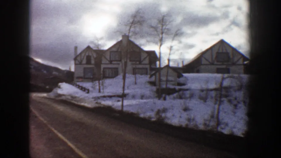 A 1961 Aspen winter driving view shows a snow-lined road beside a timber-framed house, bare trees, fence rails, and a small roofed structure.