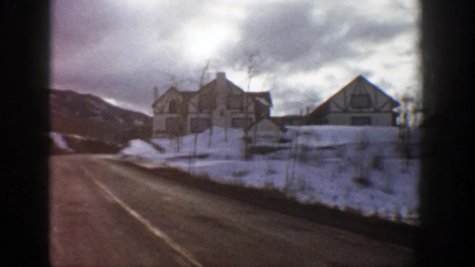 Final frame from the Aspen drive shows snowy roadside houses, bare winter trees, a fence line, and a cloudy sky over a mountain-town street.
