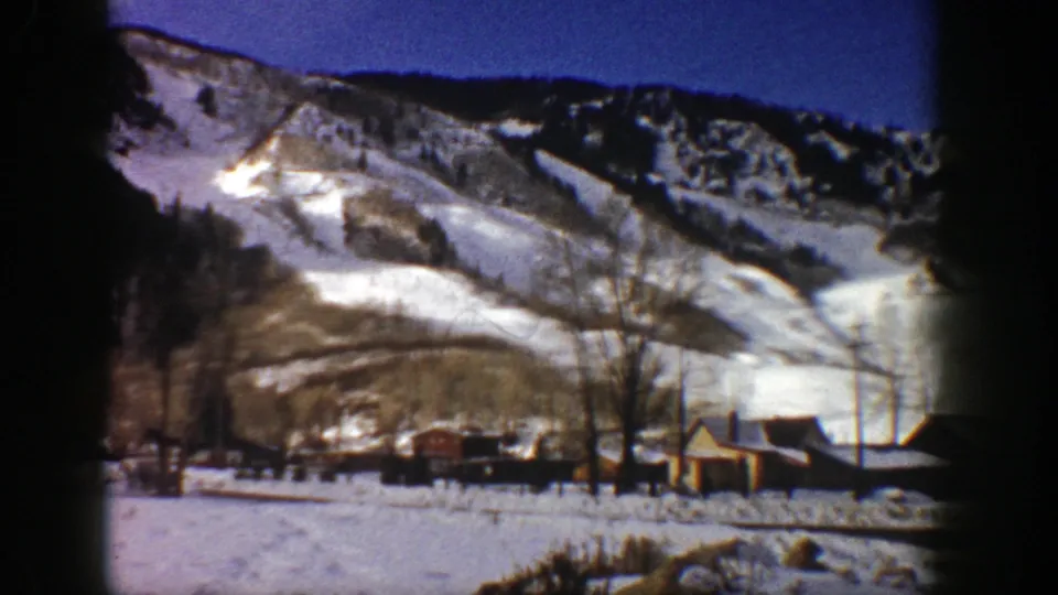 1961 Aspen winter landscape with snow-covered ski slopes, a small yellow building, bare trees, and valley snow.