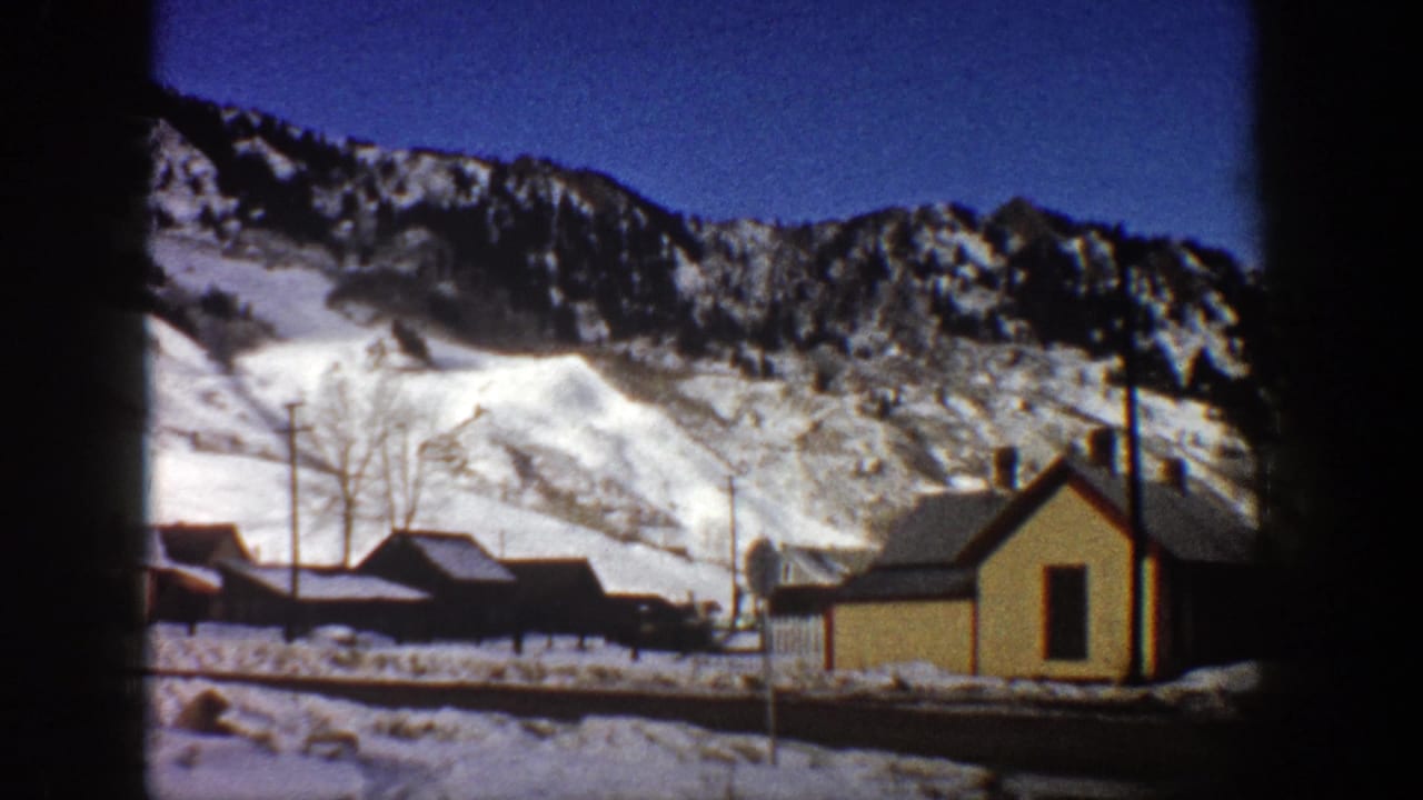 Yellow house and clustered buildings at the base of snowy mountains.
