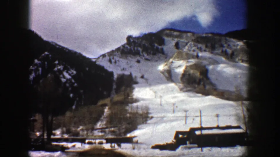 1961 Aspen, Colorado frame looking toward a snowy slope, dark roofline, leafless trees, and mountain ridges.