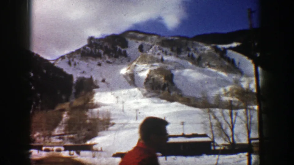 1961 Aspen winter home-movie frame with snowy slopes, buildings, bare trees, and a foreground person in profile.